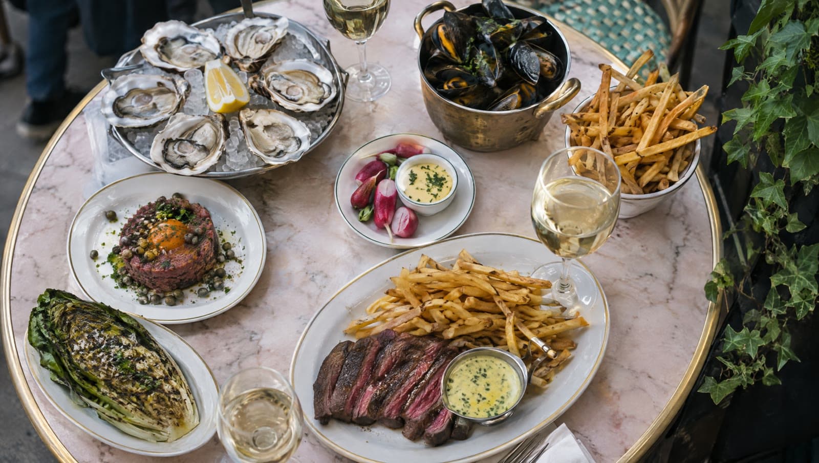 Steak frites, tatar og østers på et lyserødt marmorbord — Les Trois Cochons