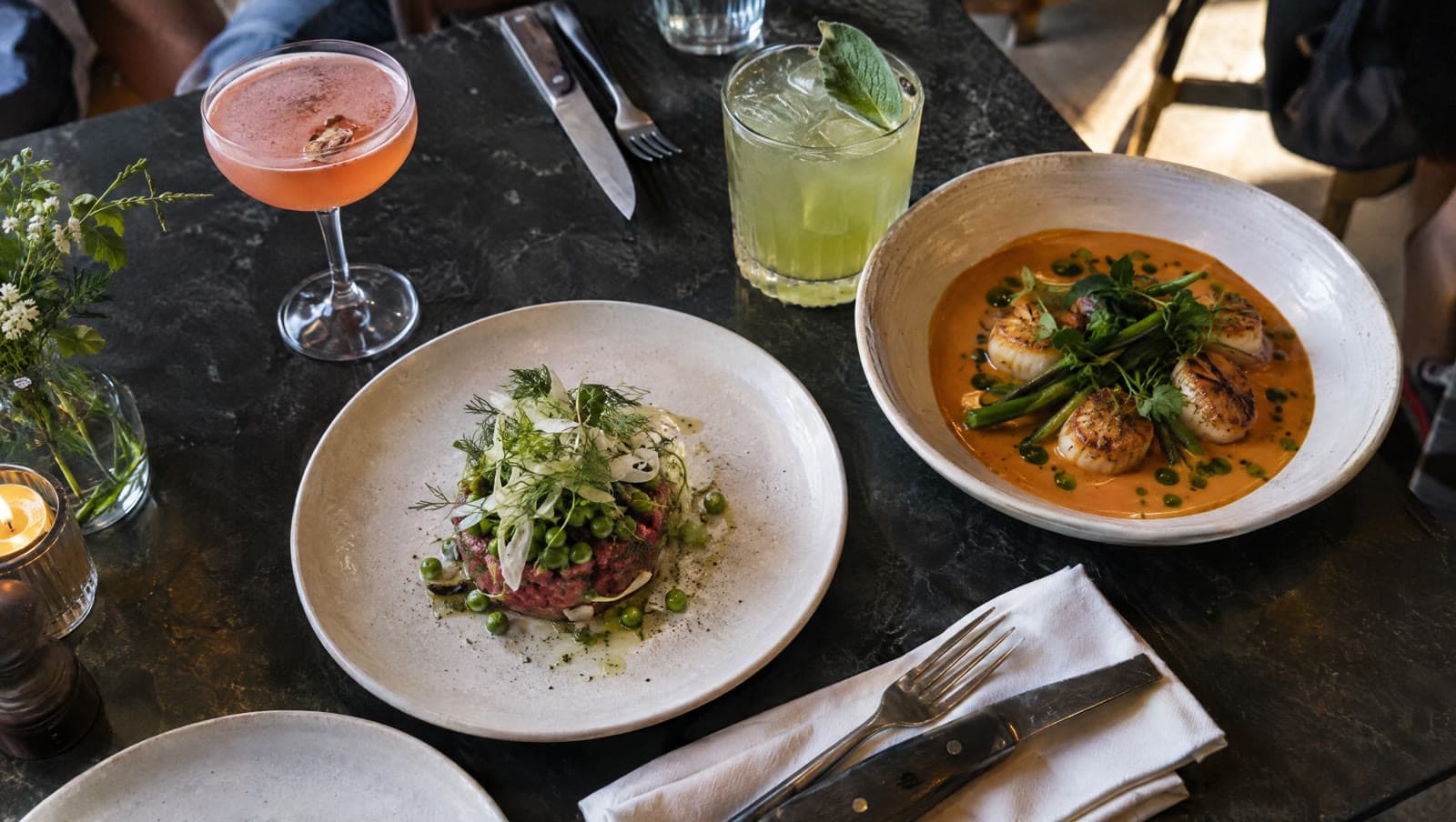 Tatar, kammuslinger i bisque og cocktails på et sort bord — Pluto